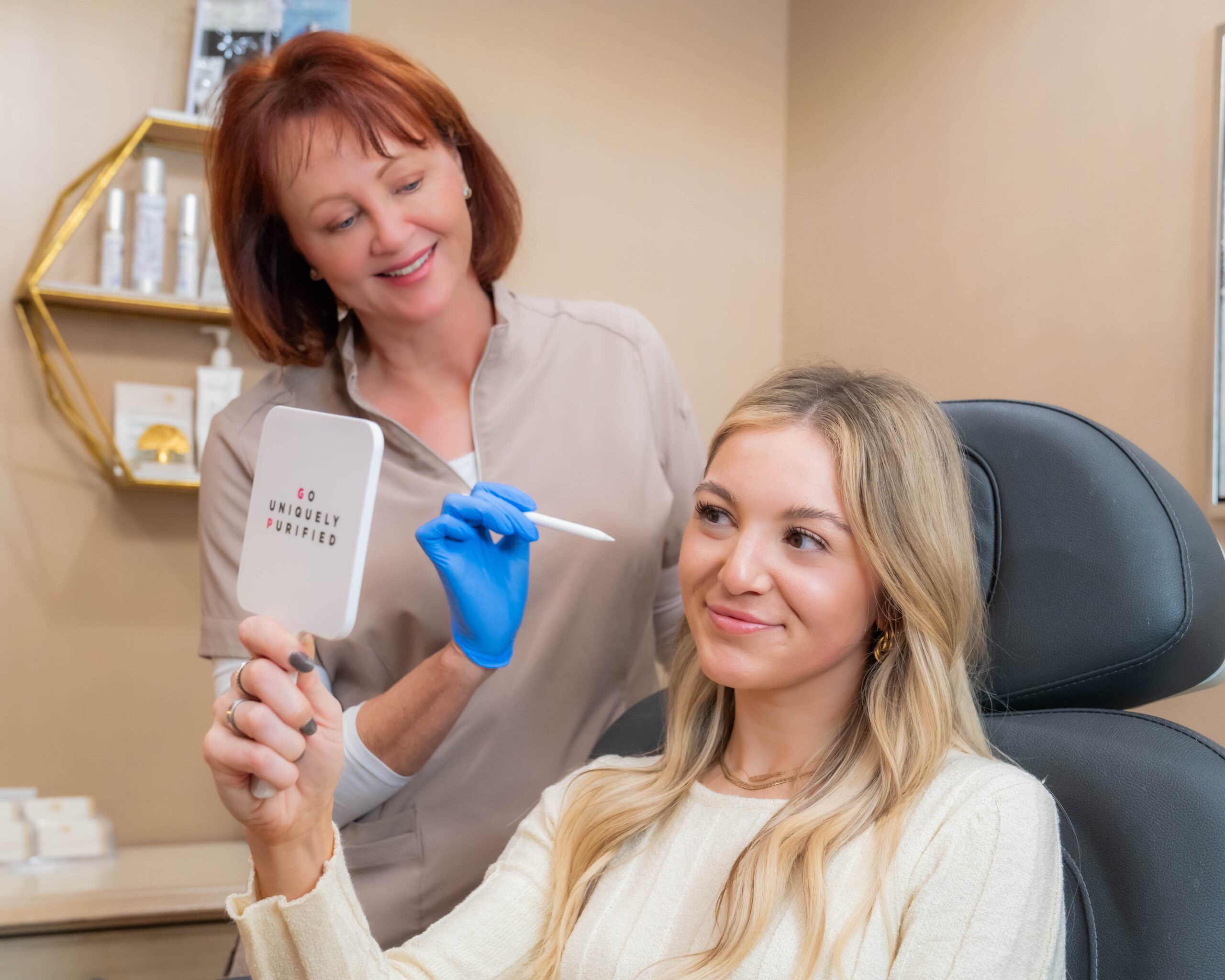 A Medical Spa Professional and her client are smiling as she inspects the results with a mirror in a private room